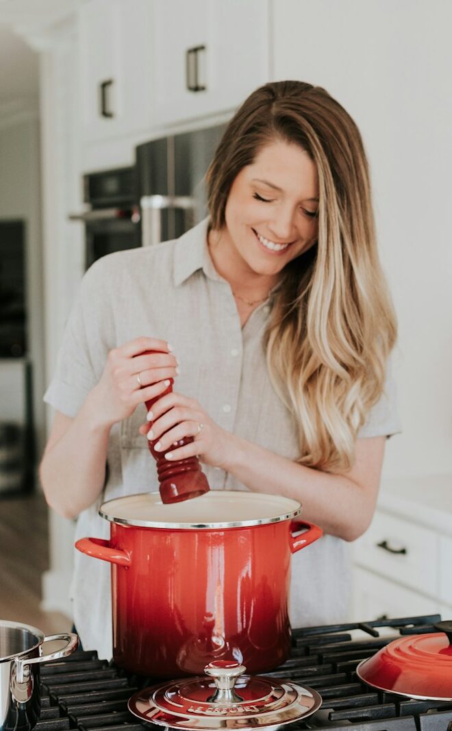smiling woman standing and putting pepper on stock pot