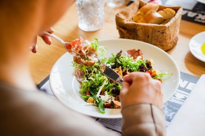 A person eating a plate full of healthy food with bread in the background