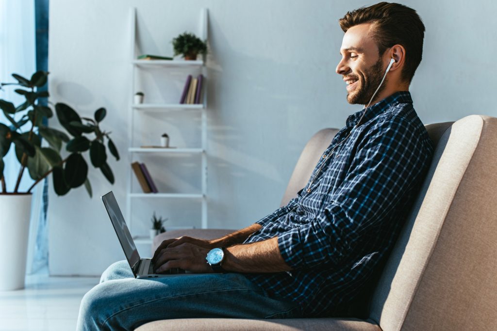 side view of smiling man in earphones taking part in webinar at home