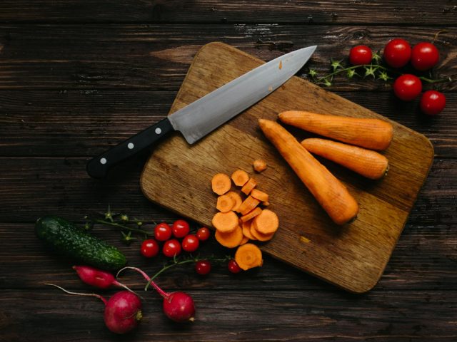 High-angle shot of fresh vegetables and kitchen knife on wooden board.