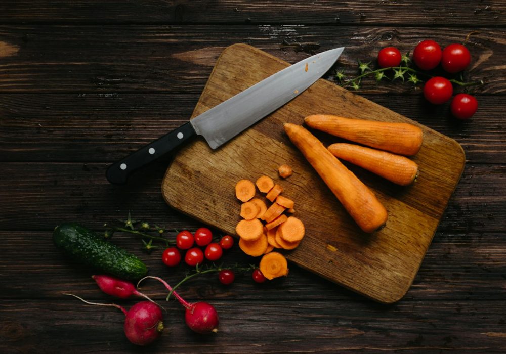 High-angle shot of fresh vegetables and kitchen knife on wooden board.