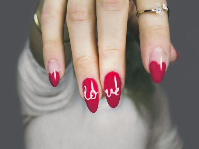 Vibrant red nails with 'love' art on a woman's hand, showcasing elegant style and design.