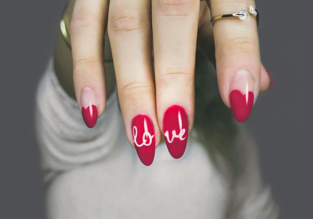 Vibrant red nails with 'love' art on a woman's hand, showcasing elegant style and design.