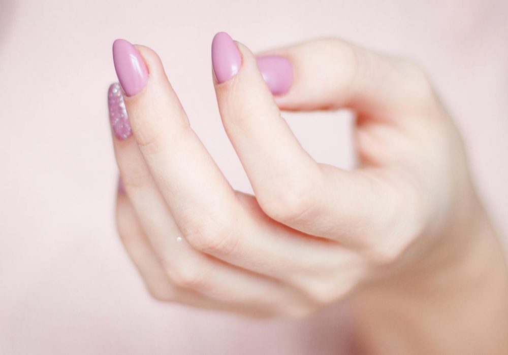 A close-up of a woman's hand showing a stylish pink and glittery manicure.