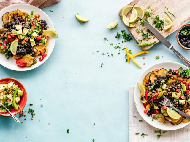Colorful Mexican salad with avocado, black beans, and lime on a light blue surface.
